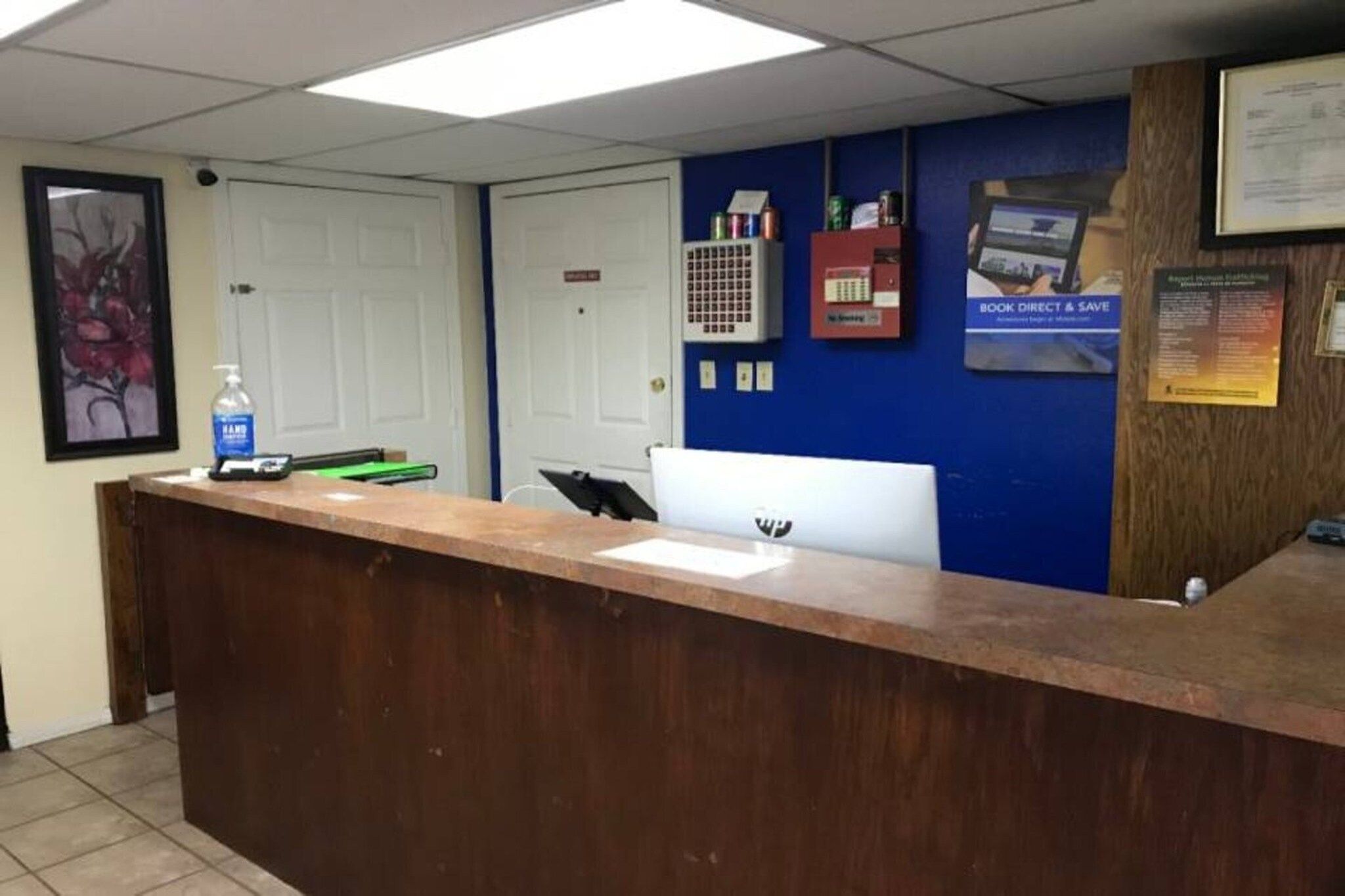 A reception desk with a computer, a water bottle, and a framed picture on the wall.