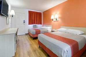 Ein Hotelzimmer mit zwei Betten, einem Schreibtisch, einem Sessel und einem Fernseher.