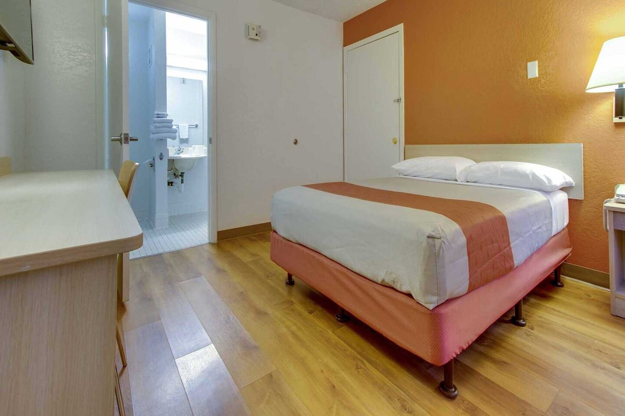 A hotel room with a bed, bedside table, and a bathroom visible through an open door.
