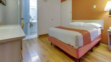 A hotel room with a bed, bedside table, and a bathroom visible through an open door.