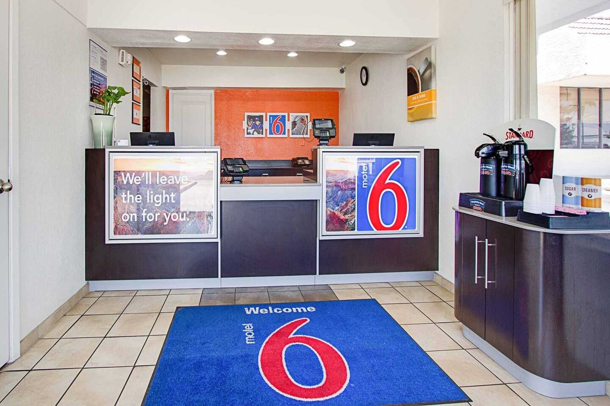 A motel reception desk with a welcome mat and a large number 6 sign.