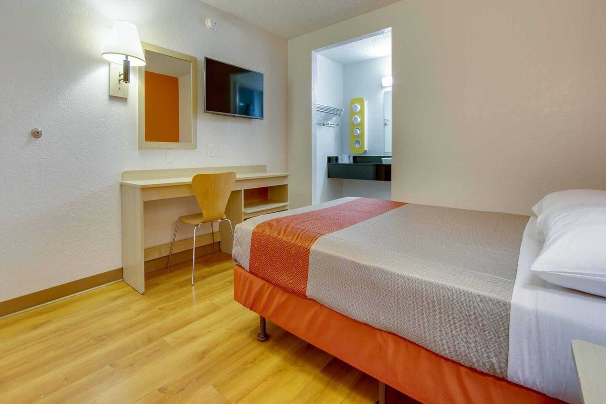 A hotel room with a bed, a desk, a chair, a television, and a bathroom mirror.
