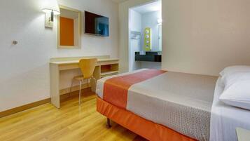 A hotel room with a bed, a desk, a chair, a television, and a bathroom mirror.