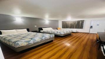 A hotel room with two beds, a wooden floor, a desk, and a chair.
