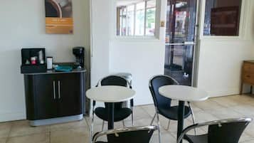 Un pequeño café con una máquina de café, dos sillas, una mesa y una barra con una taza de café.