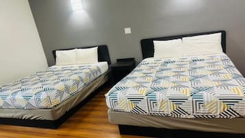 Dos camas individuales con ropa de cama estampada, suelo de madera y pared gris con una lámpara.