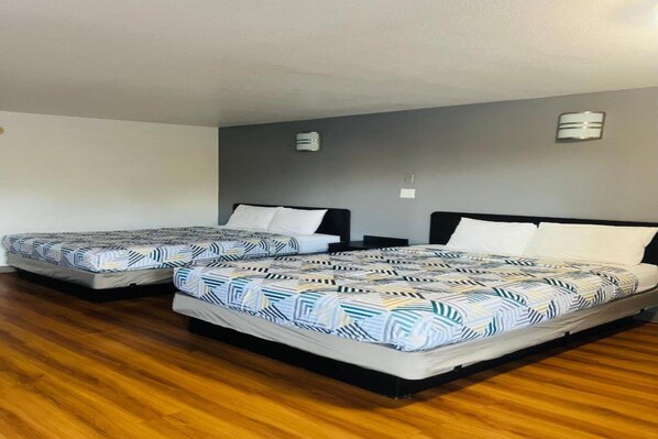 Two single beds with patterned bedding in a room with wooden flooring and grey walls.