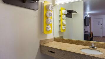 A bathroom with a granite countertop sink, a mirror, and a towel rack with multiple towels.