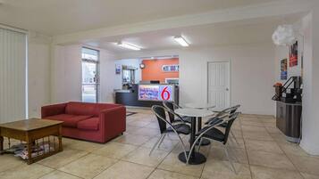 Una sala de estar con un sofá rojo, una mesa de centro y una zona de comedor con una mesa y sillas. Se observa una cocina al fondo con una encimera y un refrigerador.