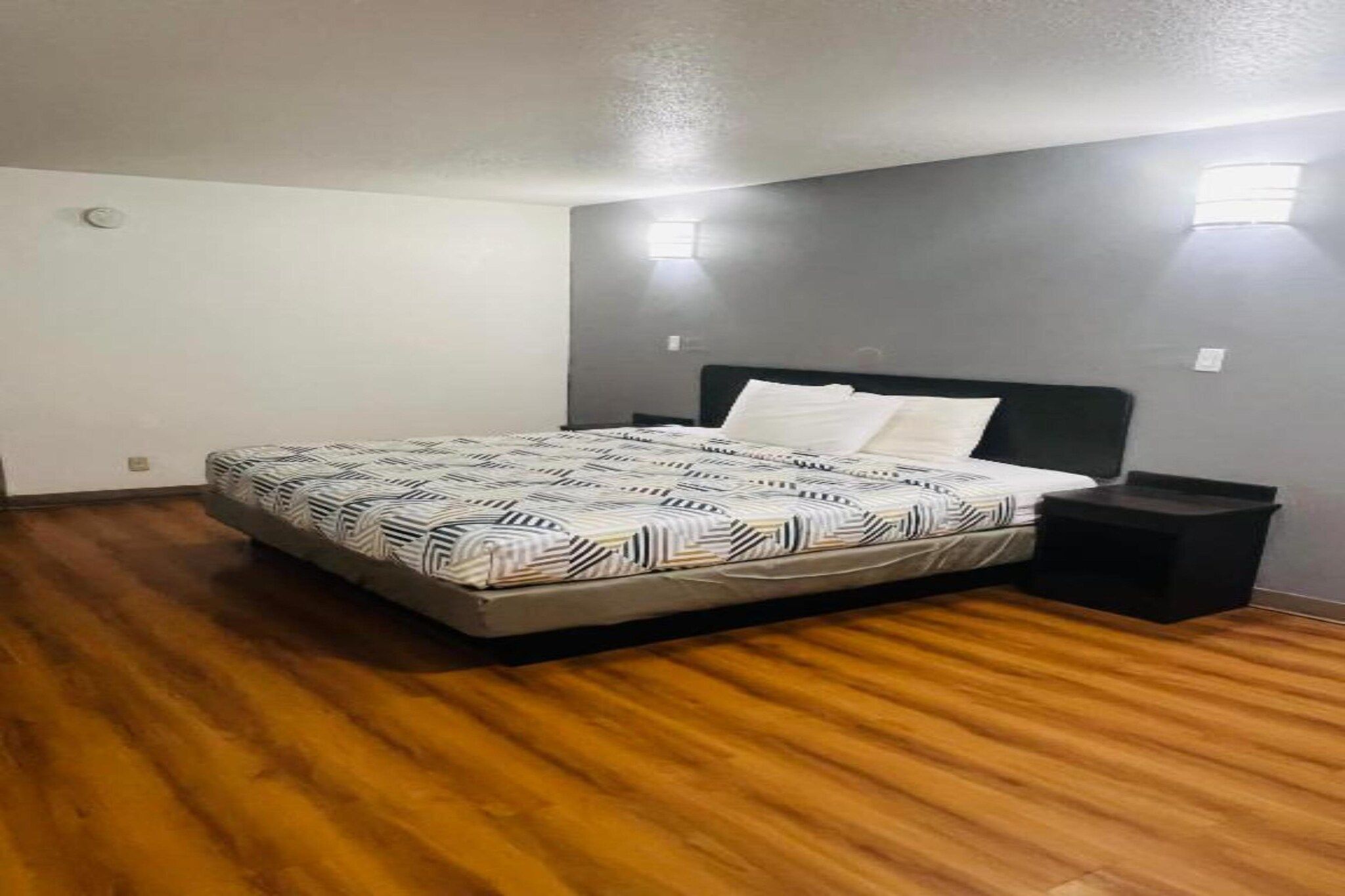 Een slaapkamer met een bed, een nachtkastje en een wandlamp.