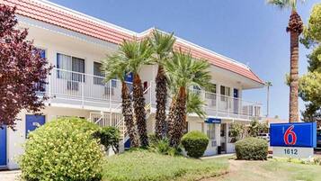 A motel with a red roof, multiple balconies, and palm trees.