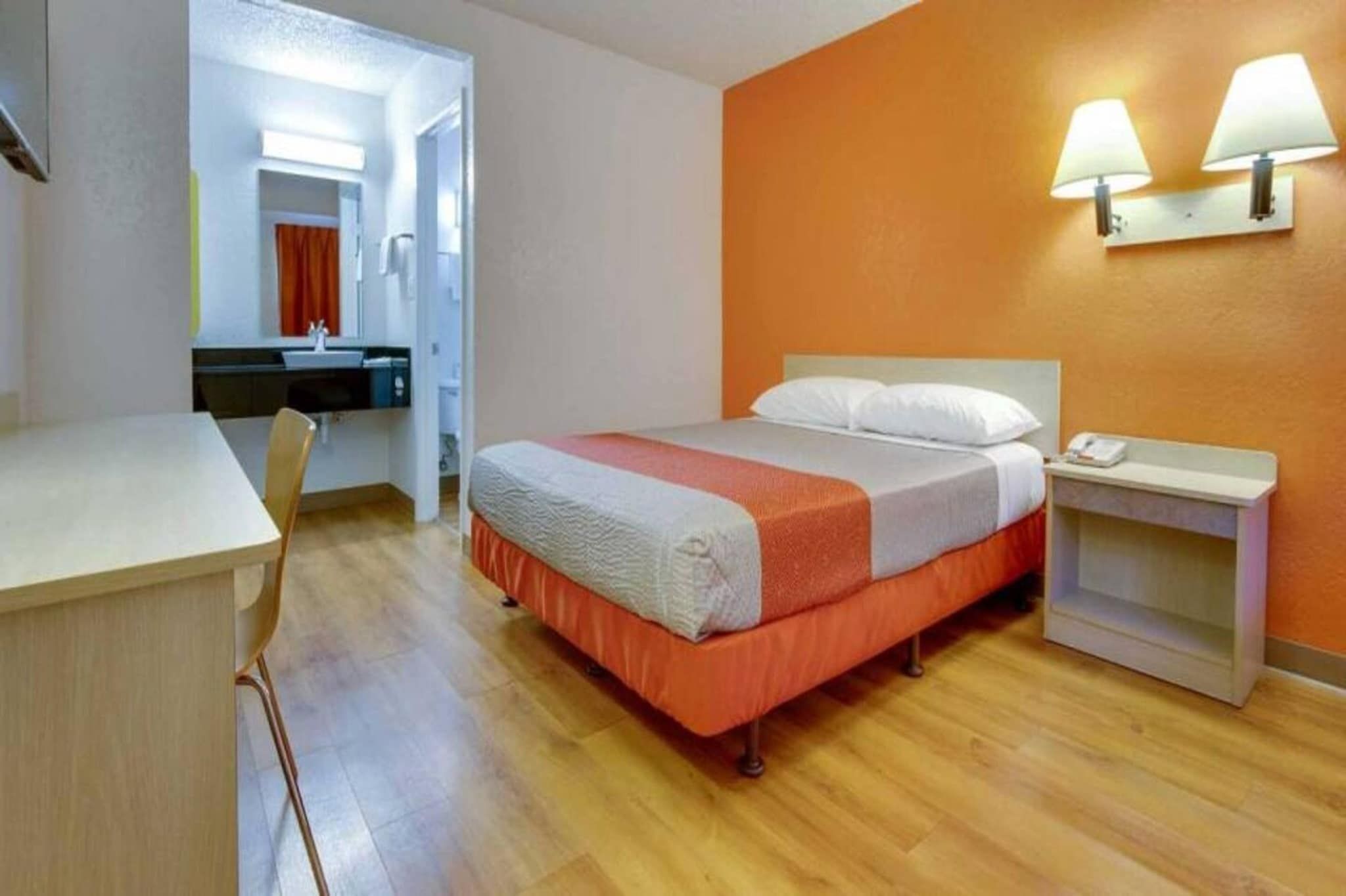 A hotel room with a bed, bedside table, and a desk with a chair.