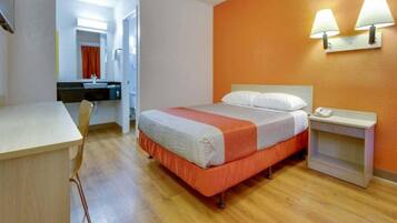 A hotel room with a bed, bedside table, and a desk with a chair.