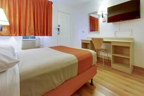 Ein Hotelzimmer mit Bett, Schreibtisch, Stuhl, Spiegel und einem Fenster mit Vorhängen.