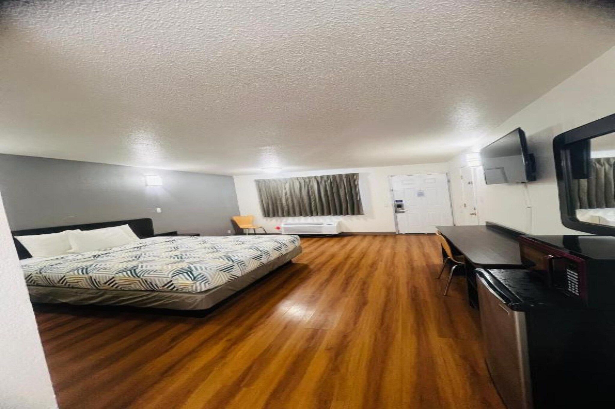 A hotel room with a bed, a desk, a chair, a television, and a door.