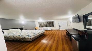 A hotel room with a bed, a desk, a chair, a television, and a door.