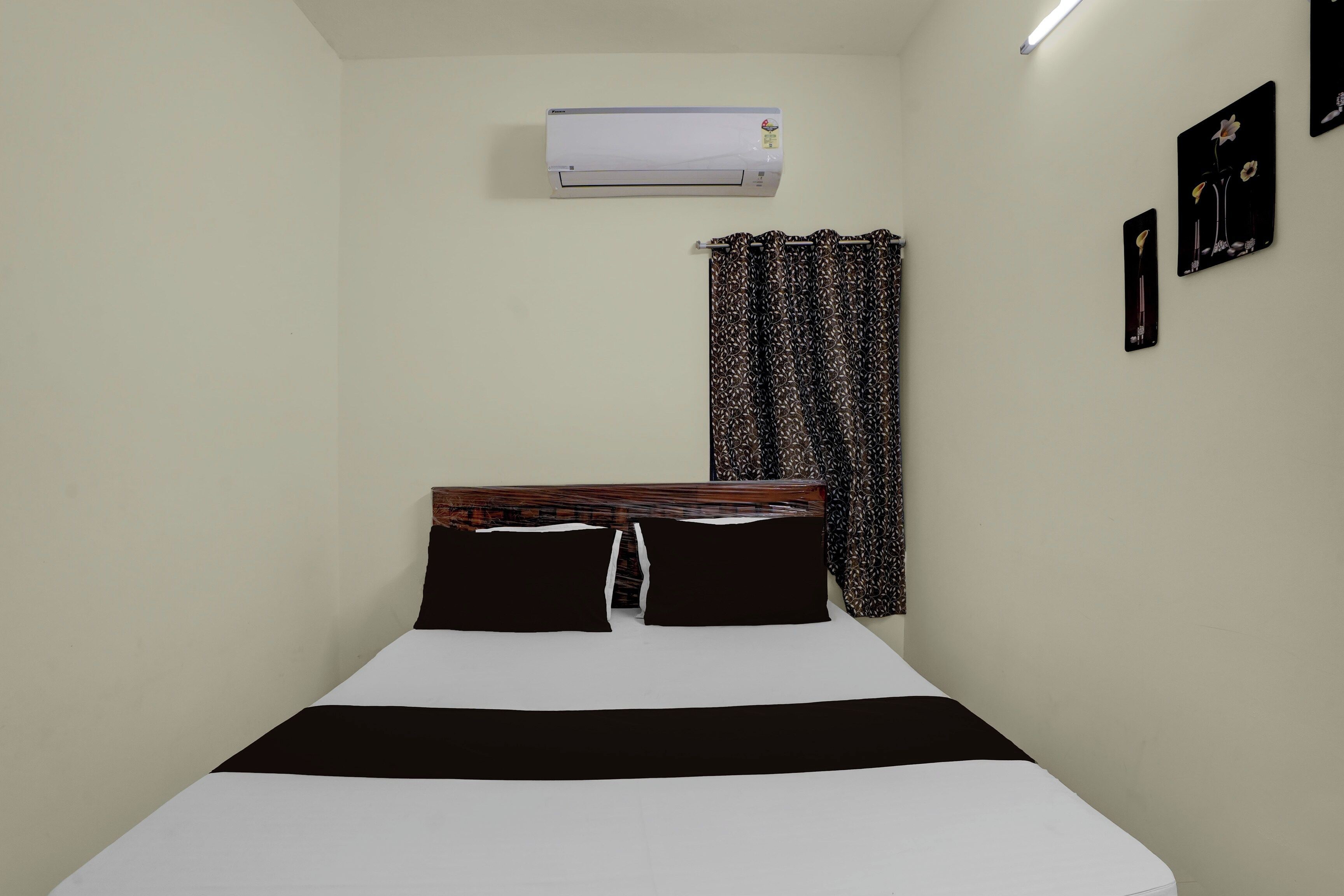 A single bed with a wooden headboard, a white and black bedspread, a patterned curtain, and a wall-mounted air conditioner.