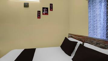 Una habitación de hotel con cama, mesita de noche, un reloj de pared y una ventana con cortina.