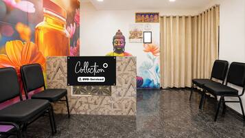 Zona de recepción con mostrador, sillas, una estatua de Buda y una pared con motivos florales y geométricos.