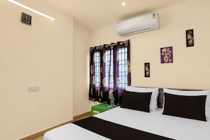 A hotel room with a bed, an air conditioner, a window with curtains, a wall-mounted clock, and a small table with a green tablecloth. - Collection O Shriram Gateway Road (Chennai)