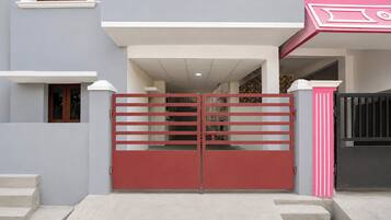 A gated entrance to a residential property with a red gate, a white door, and a pink decorative element on the right.