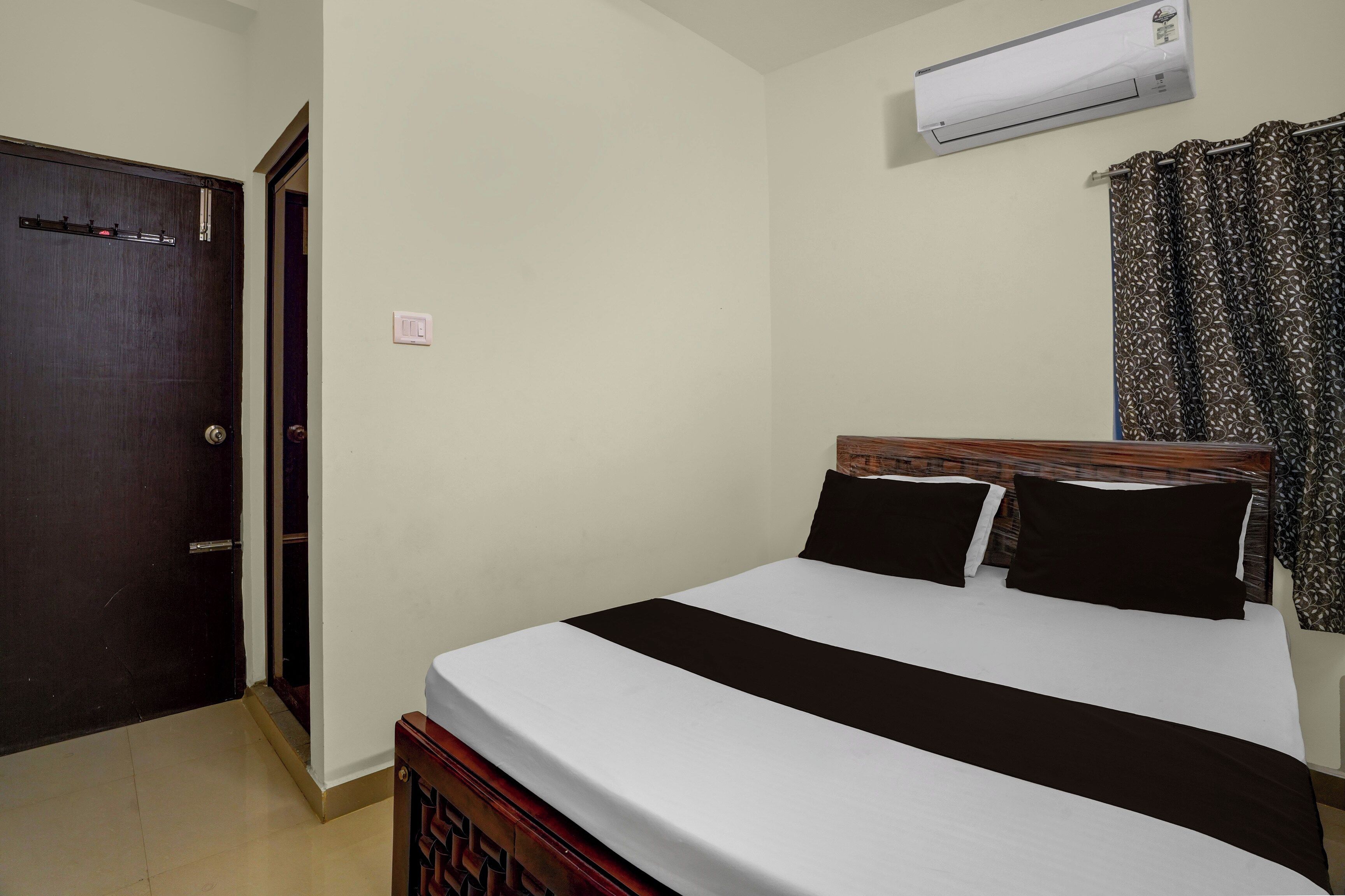 Una habitación de hotel con cama, puerta, equipo de aire acondicionado y cortina.