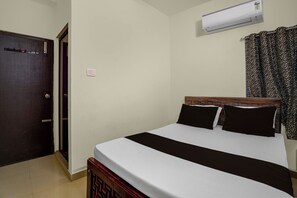 Una habitación de hotel con cama, puerta, equipo de aire acondicionado y cortina.
