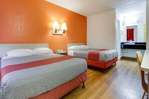 Une chambre d’hôtel avec deux lits, une table de chevet, une lampe et une salle de bain visible au fond.