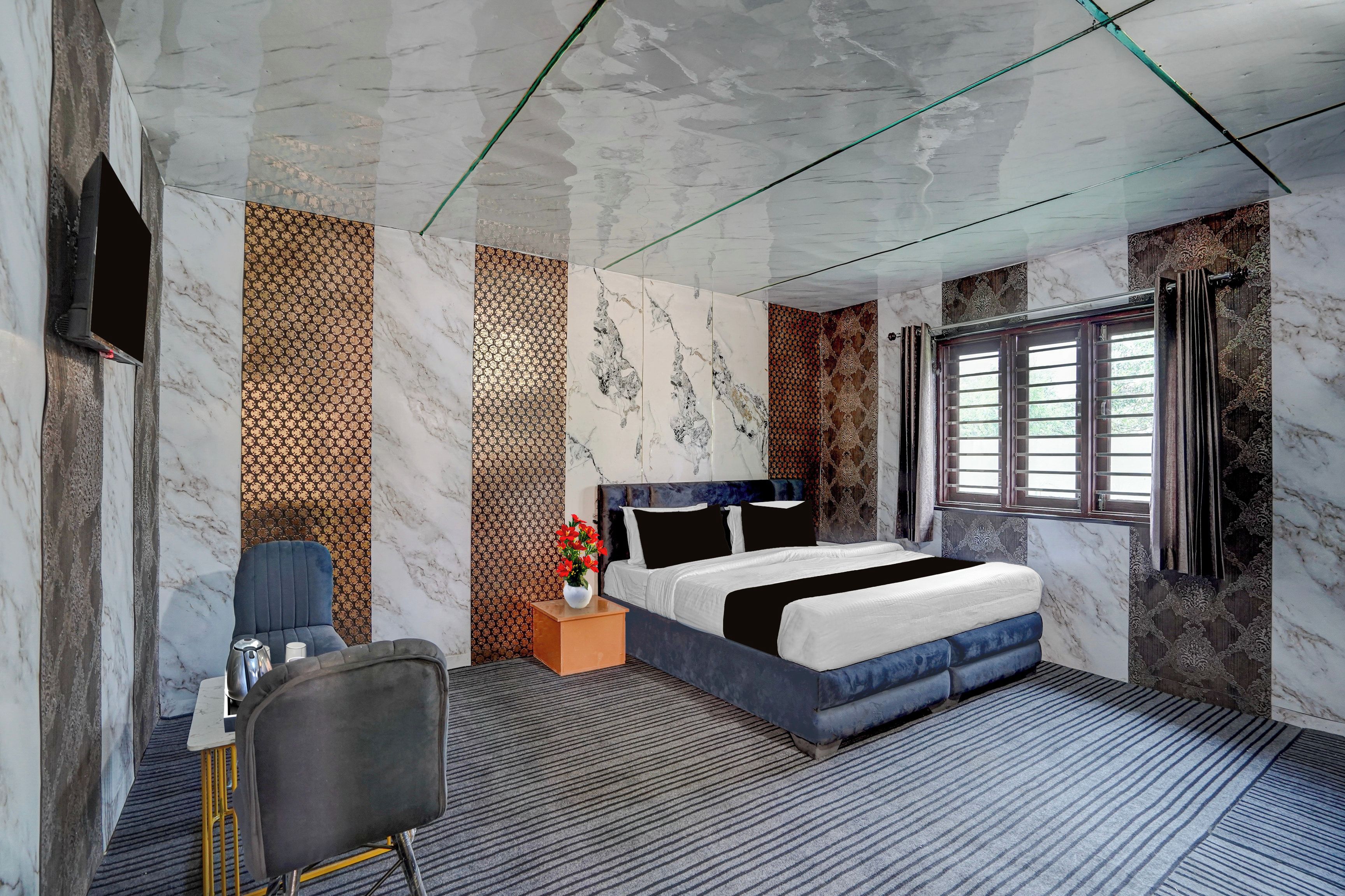Quarto de hotel com cama, escrivaninha, cadeira, vaso com flores e janela com cortinas.