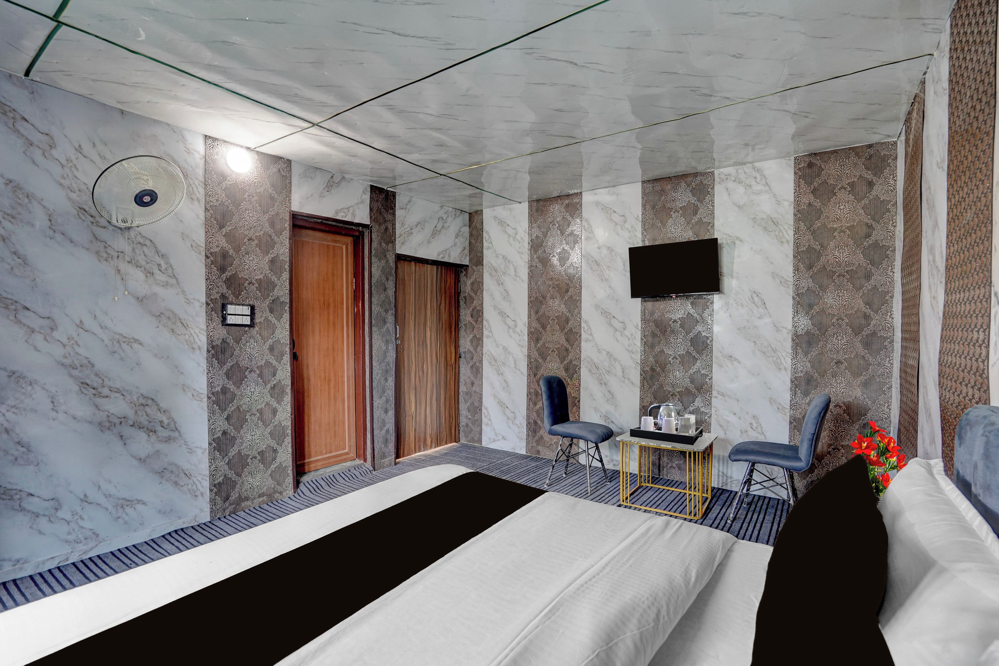 A hotel room with a bed, two chairs, a small table, a TV, and a door.