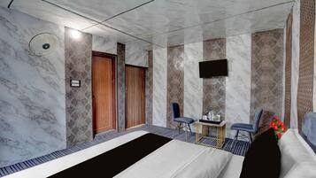 A hotel room with a bed, two chairs, a small table, a TV, and a door.
