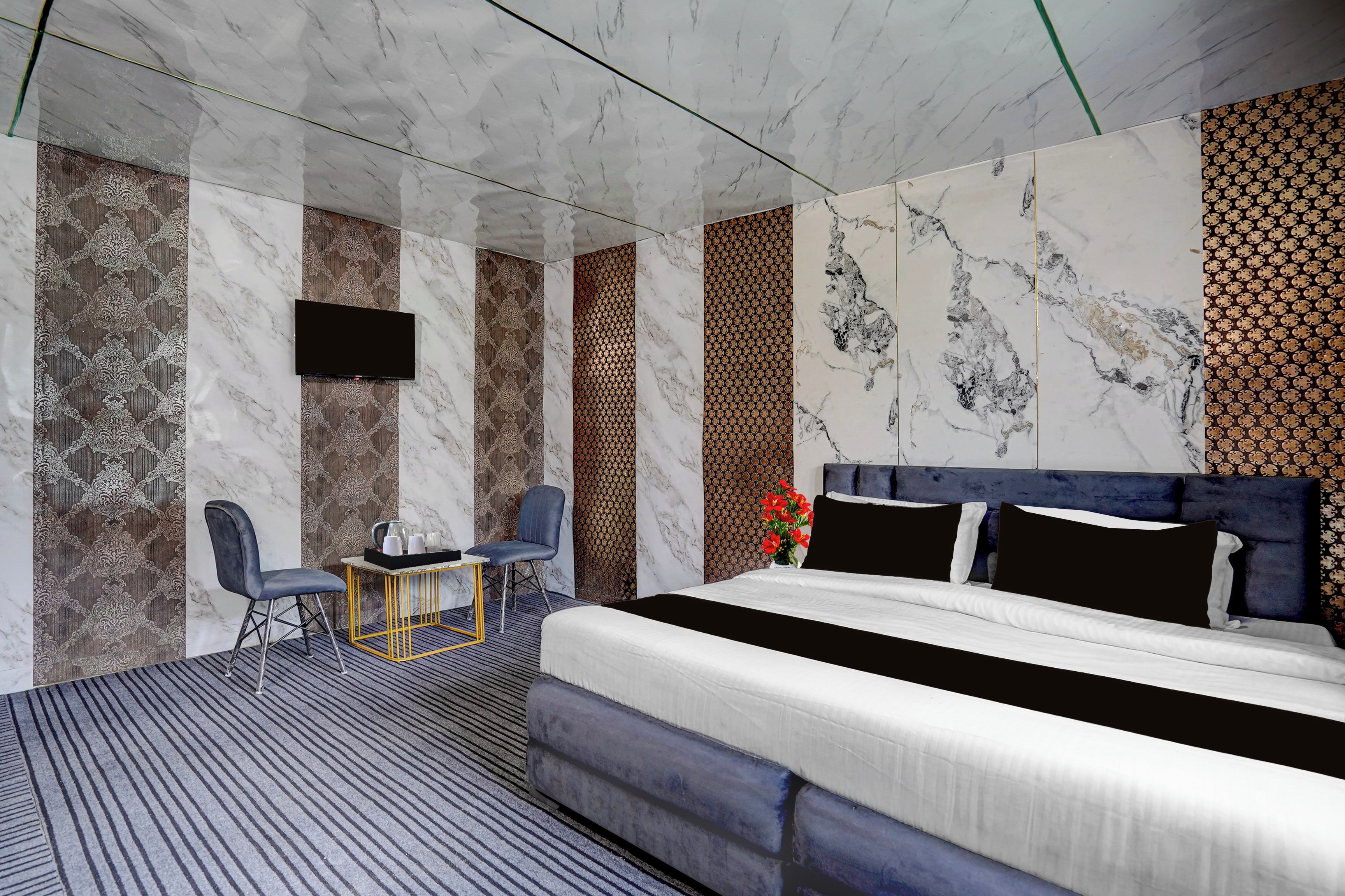 Una habitación de hotel moderna con una cama grande, un televisor de pantalla plana montado en la pared, una pequeña mesa con sillas y un panel decorativo en la pared.