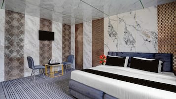 Una habitación de hotel moderna con una cama grande, un televisor de pantalla plana montado en la pared, una pequeña mesa con sillas y un panel decorativo en la pared.