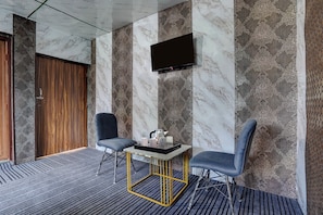 A modern hotel room with a marble wall, a flat-screen TV, two armchairs, a small table with a tray, and a wooden door. - Hotel O Sahaspur Dehradun (Vikasnagar)
