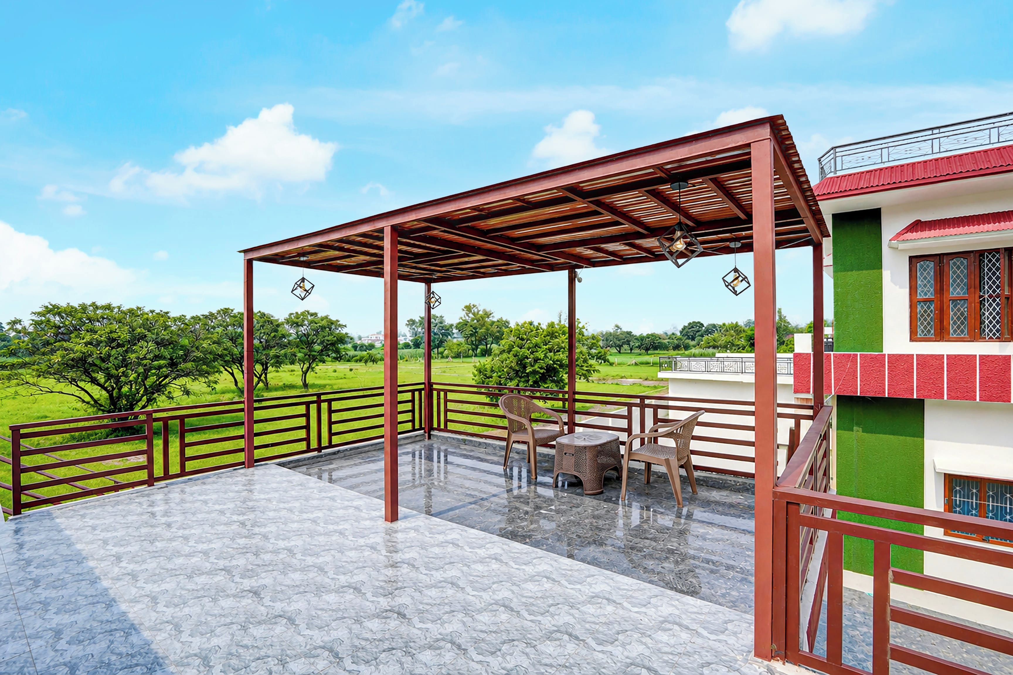 A covered outdoor area with a patio, chairs, and a view of a green landscape.