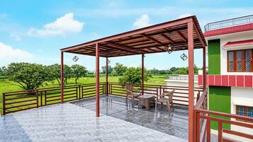 A covered outdoor area with a patio, chairs, and a view of a green landscape.