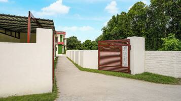 A pathway leading to a gated entrance with a building on the left and a white wall on the right.