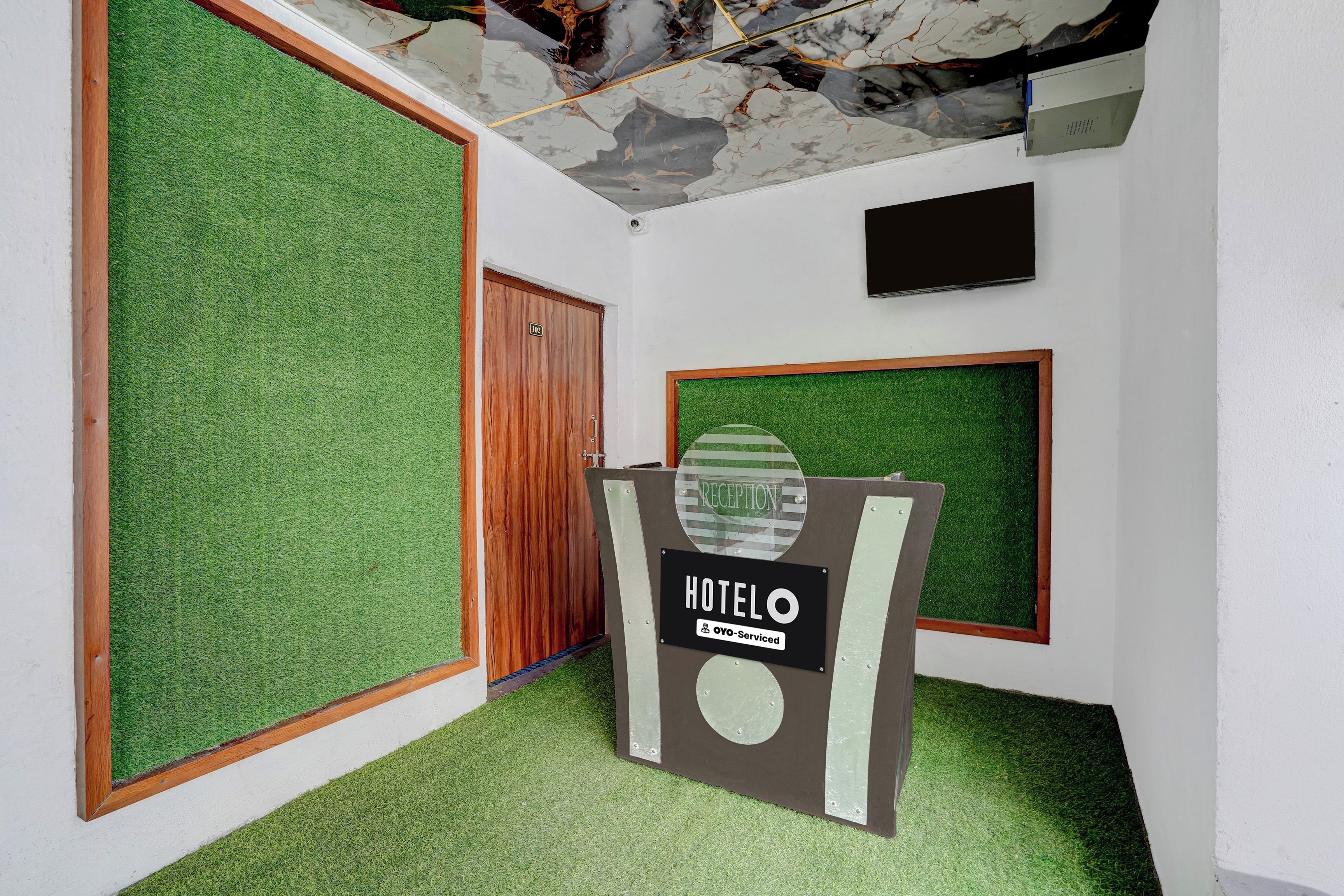 Zona de recepción de hotel con suelo de césped artificial, un mostrador de recepción y una puerta de madera.