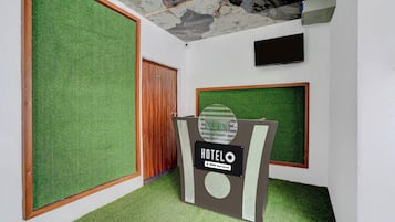 Zona de recepción de hotel con suelo de césped artificial, un mostrador de recepción y una puerta de madera.