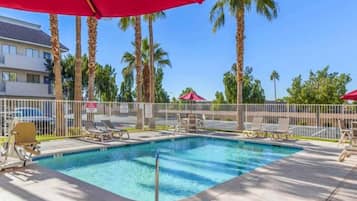 A rectangular swimming pool with a fenced area, surrounded by palm trees and lounge chairs.