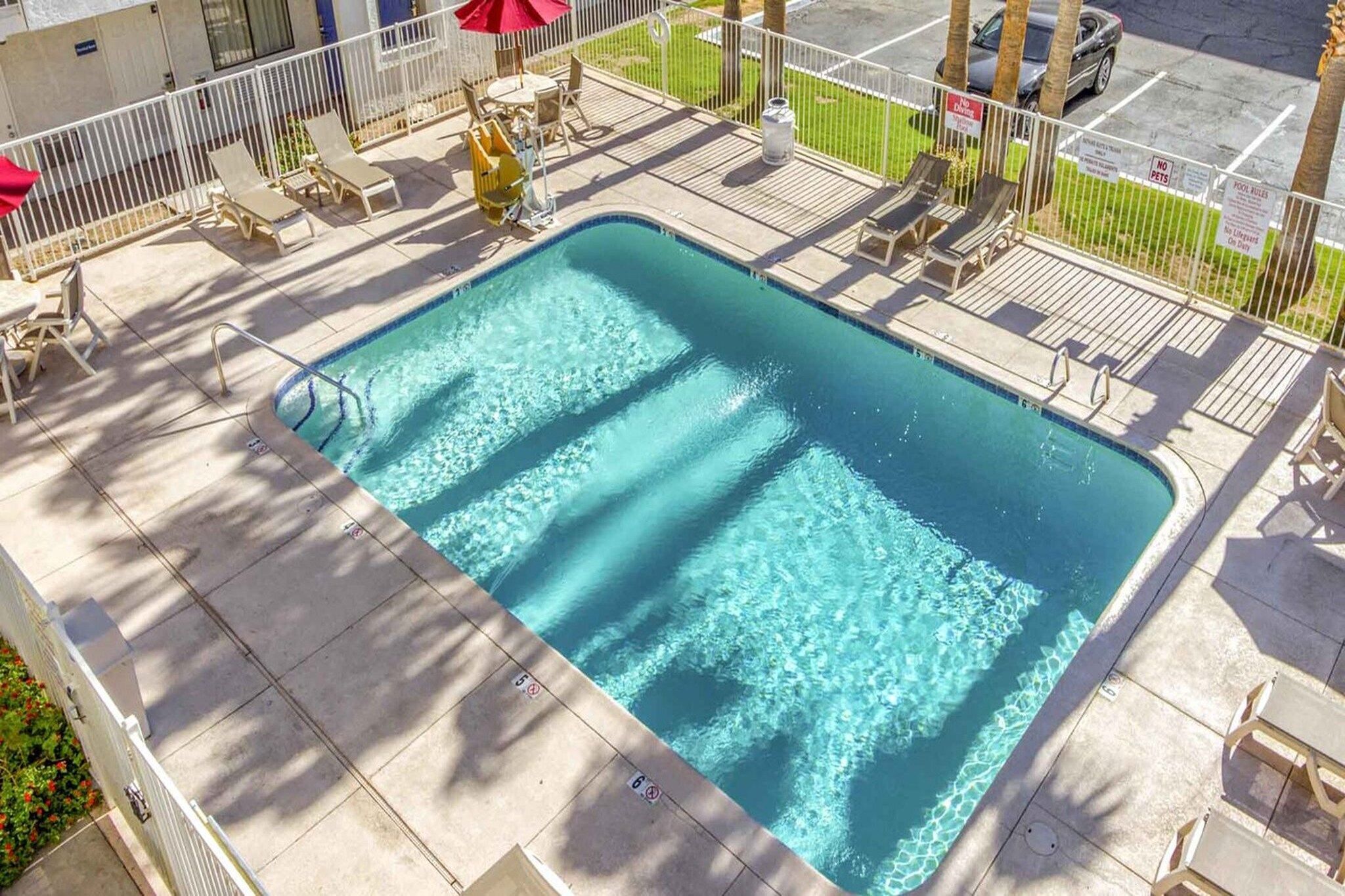A rectangular swimming pool with a tiled deck, surrounded by lounge chairs and umbrellas.