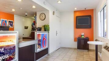 Een hotel receptie met een klok, een bord met het nummer 6, en een kleine tafel met een stoel.