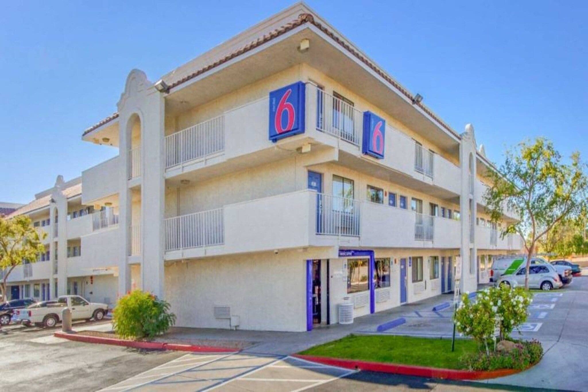 A multi-story hotel with a prominent '6' sign, a covered entrance, and a parking lot.