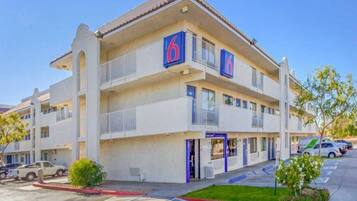 A multi-story hotel with a prominent '6' sign, a covered entrance, and a parking lot.