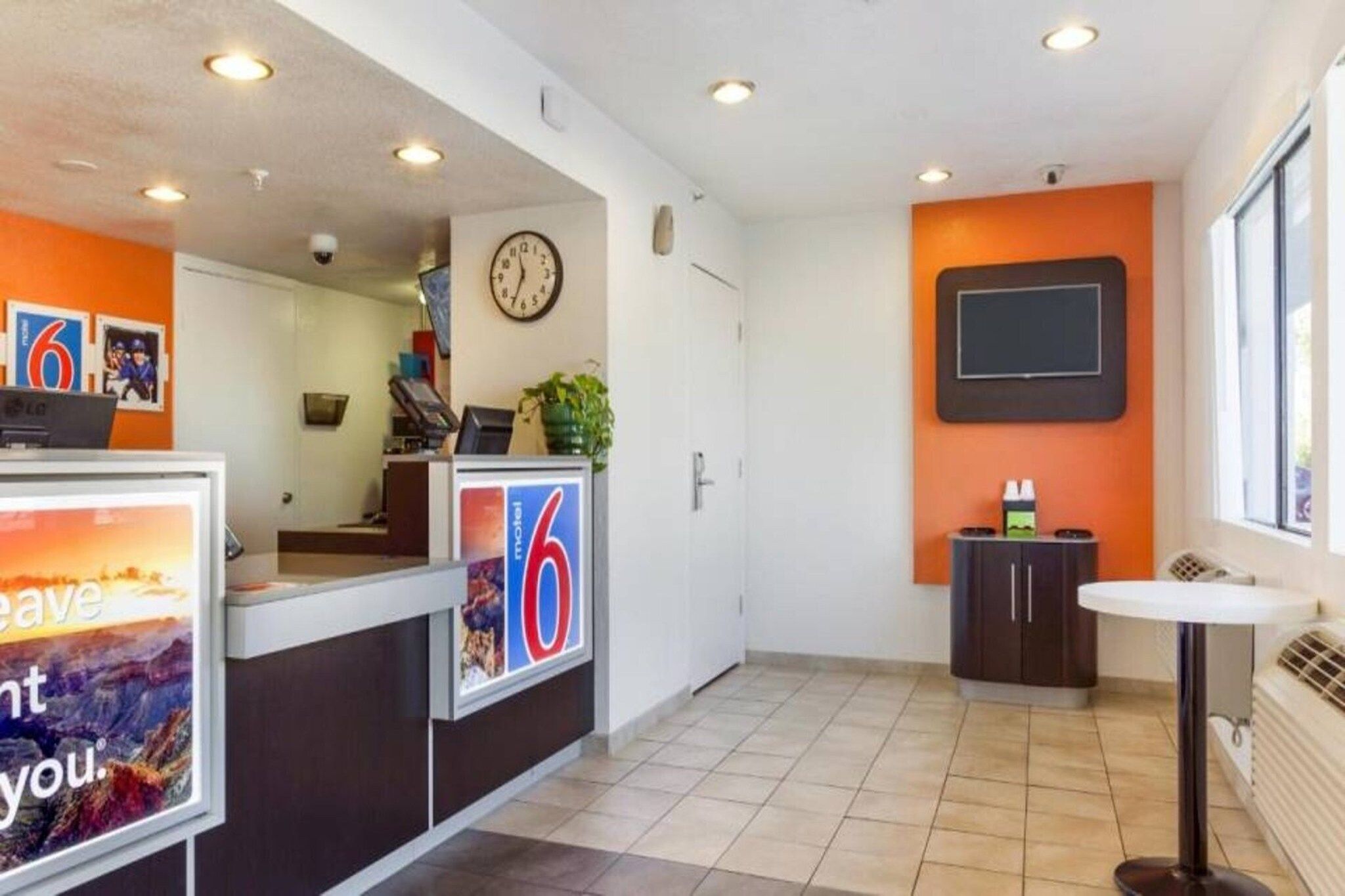 A hotel reception area with a clock, a digital display, and a small seating area.