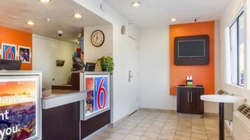 A hotel reception area with a clock, a digital display, and a small seating area.