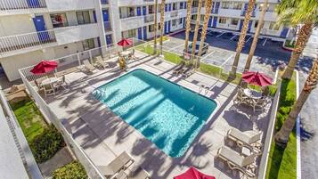 A swimming pool surrounded by lounge chairs and umbrellas, with a multi-story building in the background.