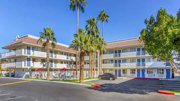 A multi-story motel with a parking lot, palm trees, and a clear blue sky.