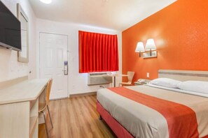 Una habitación de hotel con cama, escritorio, silla y televisor.