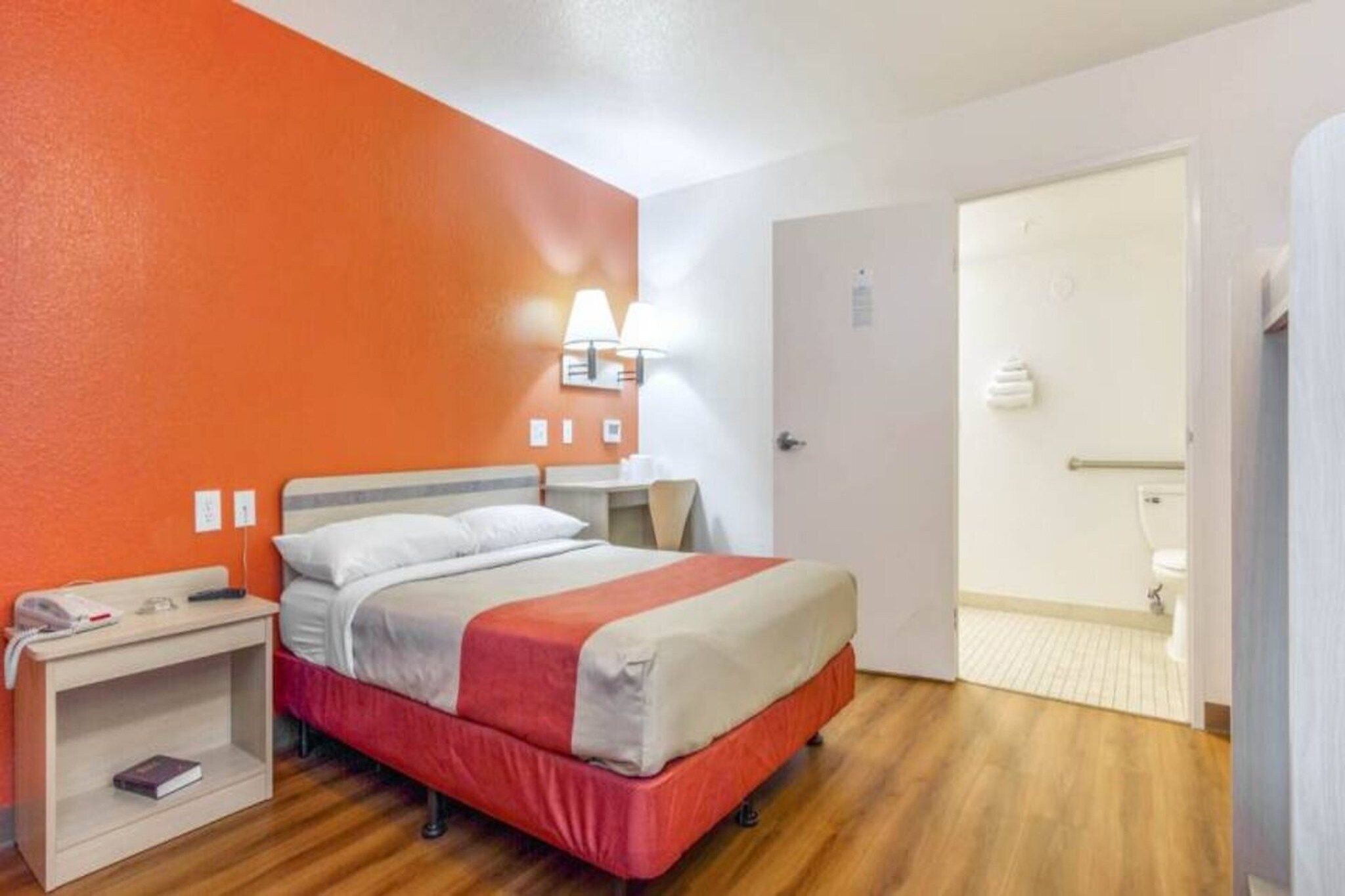 Une chambre d’hôtel comprenant un lit, une table de chevet, une lampe et une porte donnant accès à une salle de bain.